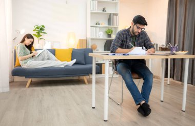 Evde kız arkadaşıyla bilgisayarla çalışırken gülümseyen genç bir serbest çalışanın portresi.