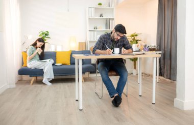 Evde kız arkadaşıyla bilgisayarla çalışırken gülümseyen genç bir serbest çalışanın portresi.