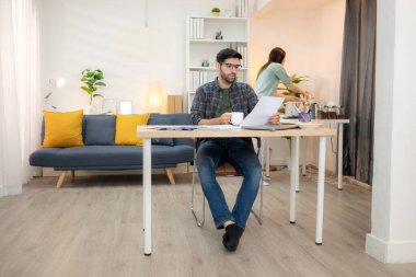 Evde kız arkadaşıyla bilgisayarla çalışırken gülümseyen genç bir serbest çalışanın portresi.