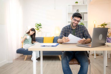 Evde kız arkadaşıyla bilgisayarla çalışırken gülümseyen genç bir serbest çalışanın portresi.