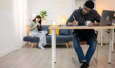 Evde kız arkadaşıyla bilgisayarla çalışırken gülümseyen genç bir serbest çalışanın portresi.