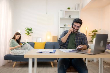 Evde kız arkadaşıyla bilgisayarla çalışırken gülümseyen genç bir serbest çalışanın portresi.