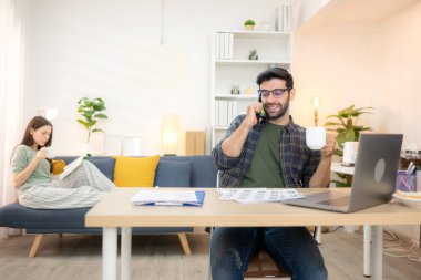 Evde kız arkadaşıyla bilgisayarla çalışırken gülümseyen genç bir serbest çalışanın portresi.