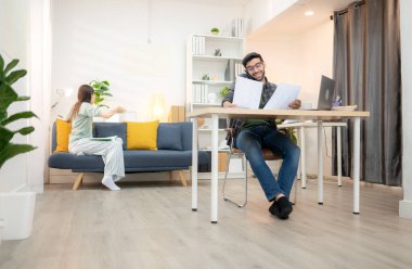 Evde kız arkadaşıyla bilgisayarla çalışırken gülümseyen genç bir serbest çalışanın portresi.