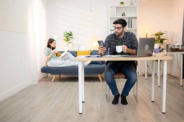 Evde kız arkadaşıyla bilgisayarla çalışırken gülümseyen genç bir serbest çalışanın portresi.