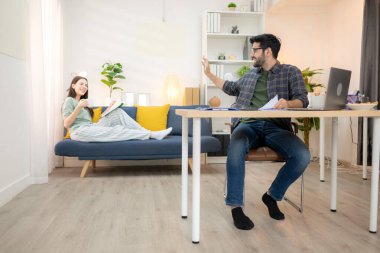 Evde kız arkadaşıyla bilgisayarla çalışırken gülümseyen genç bir serbest çalışanın portresi.