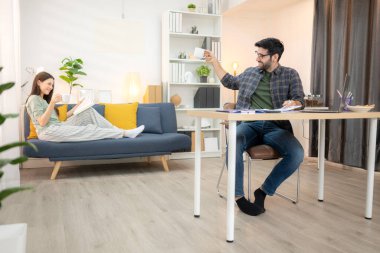 Evde kız arkadaşıyla bilgisayarla çalışırken gülümseyen genç bir serbest çalışanın portresi.