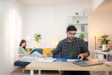 Evde kız arkadaşıyla bilgisayarla çalışırken gülümseyen genç bir serbest çalışanın portresi.