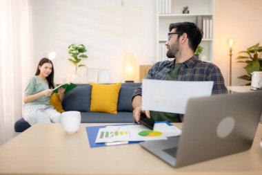 Evde kız arkadaşıyla bilgisayarla çalışırken gülümseyen genç bir serbest çalışanın portresi.