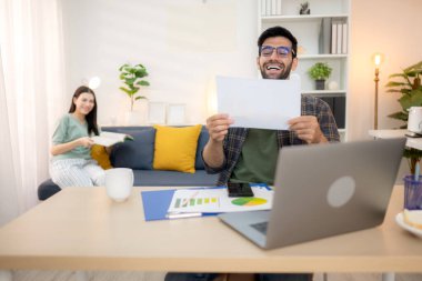 Evde kız arkadaşıyla bilgisayarla çalışırken gülümseyen genç bir serbest çalışanın portresi.