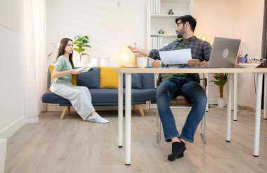 Evde kız arkadaşıyla bilgisayarla çalışırken gülümseyen genç bir serbest çalışanın portresi.