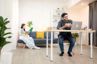 Evde kız arkadaşıyla bilgisayarla çalışırken gülümseyen genç bir serbest çalışanın portresi.