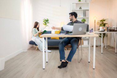 Evde kız arkadaşıyla bilgisayarla çalışırken gülümseyen genç bir serbest çalışanın portresi.