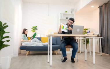 Evde kız arkadaşıyla bilgisayarla çalışırken gülümseyen genç bir serbest çalışanın portresi.