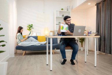 Evde kız arkadaşıyla bilgisayarla çalışırken gülümseyen genç bir serbest çalışanın portresi.