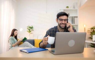 Evde kız arkadaşıyla bilgisayarla çalışırken gülümseyen genç bir serbest çalışanın portresi.