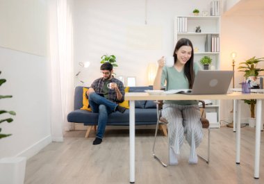 Evde erkek arkadaşıyla dizüstü bilgisayarla çalışırken gülümseyen genç bir serbest çalışanın portresi.