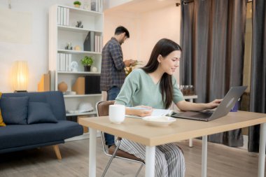 Evde erkek arkadaşıyla dizüstü bilgisayarla çalışırken gülümseyen genç bir serbest çalışanın portresi.