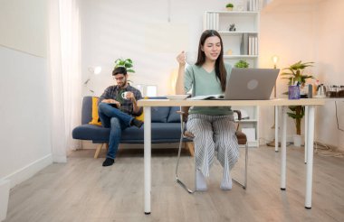 Evde erkek arkadaşıyla dizüstü bilgisayarla çalışırken gülümseyen genç bir serbest çalışanın portresi.