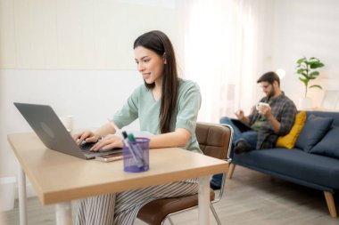 Evde erkek arkadaşıyla dizüstü bilgisayarla çalışırken gülümseyen genç bir serbest çalışanın portresi.