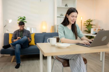 Evde erkek arkadaşıyla dizüstü bilgisayarla çalışırken gülümseyen genç bir serbest çalışanın portresi.