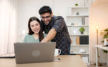 Evde erkek arkadaşıyla dizüstü bilgisayarla çalışırken gülümseyen genç bir serbest çalışanın portresi.