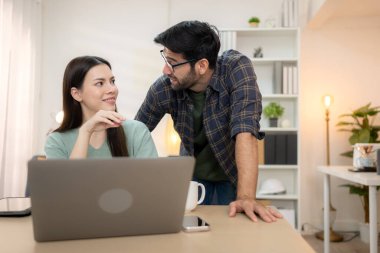 Evde erkek arkadaşıyla dizüstü bilgisayarla çalışırken gülümseyen genç bir serbest çalışanın portresi.