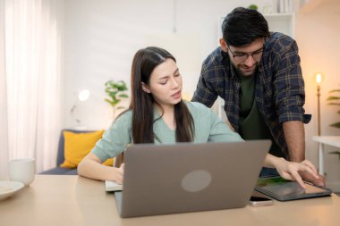 Evde erkek arkadaşıyla dizüstü bilgisayarla çalışırken gülümseyen genç bir serbest çalışanın portresi.