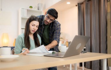 Evde erkek arkadaşıyla dizüstü bilgisayarla çalışırken gülümseyen genç bir serbest çalışanın portresi.