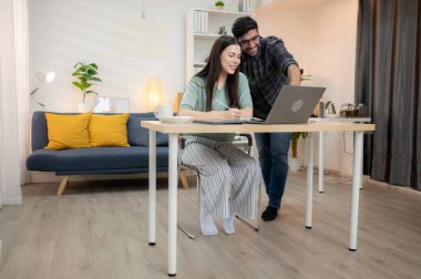 Evde erkek arkadaşıyla dizüstü bilgisayarla çalışırken gülümseyen genç bir serbest çalışanın portresi.