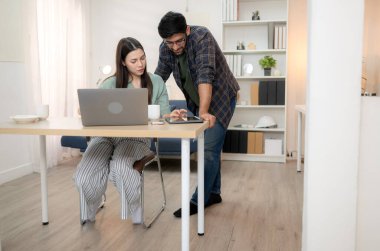 Evde erkek arkadaşıyla dizüstü bilgisayarla çalışırken gülümseyen genç bir serbest çalışanın portresi.