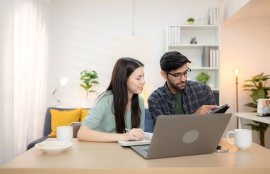 Evde erkek arkadaşıyla dizüstü bilgisayarla çalışırken gülümseyen genç bir serbest çalışanın portresi.