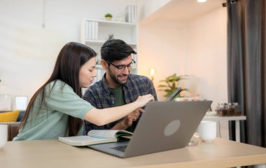 Evde erkek arkadaşıyla dizüstü bilgisayarla çalışırken gülümseyen genç bir serbest çalışanın portresi.