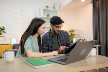 Evde erkek arkadaşıyla dizüstü bilgisayarla çalışırken gülümseyen genç bir serbest çalışanın portresi.