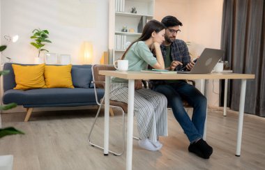 Evde erkek arkadaşıyla dizüstü bilgisayarla çalışırken gülümseyen genç bir serbest çalışanın portresi.