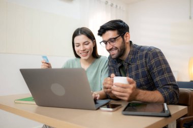 Evde erkek arkadaşıyla dizüstü bilgisayarla çalışırken gülümseyen genç bir serbest çalışanın portresi.