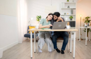 Evde erkek arkadaşıyla dizüstü bilgisayarla çalışırken gülümseyen genç bir serbest çalışanın portresi.