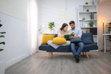 Genç çift rahatlarken gülümsüyor ve evdeki oturma odasında dizüstü bilgisayarla çalışıyorlar.