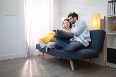 Genç çift rahatlarken gülümsüyor ve evdeki oturma odasında dizüstü bilgisayarla çalışıyorlar.