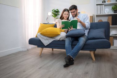 Genç çift rahatlarken gülümsüyor ve evdeki oturma odasında dizüstü bilgisayarla çalışıyorlar.