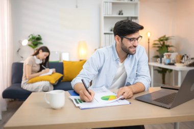 Evde dizüstü bilgisayarla çalışırken gülümseyen genç bir serbest çalışanın portresi