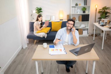 Evde kız arkadaşıyla bilgisayarla çalışırken gülümseyen genç bir serbest çalışanın portresi.