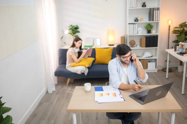 Evde kız arkadaşıyla bilgisayarla çalışırken gülümseyen genç bir serbest çalışanın portresi.