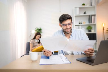 Evde kız arkadaşıyla bilgisayarla çalışırken gülümseyen genç bir serbest çalışanın portresi.