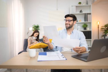 Evde kız arkadaşıyla bilgisayarla çalışırken gülümseyen genç bir serbest çalışanın portresi.