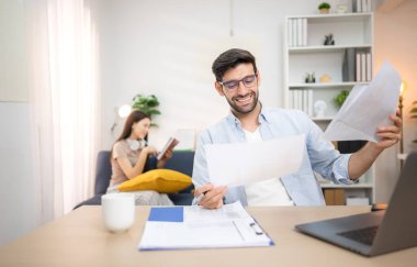 Evde kız arkadaşıyla bilgisayarla çalışırken gülümseyen genç bir serbest çalışanın portresi.