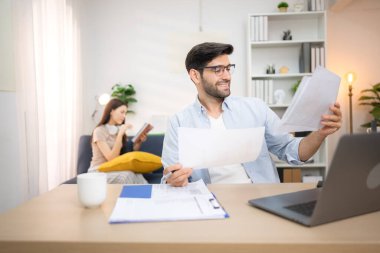 Evde kız arkadaşıyla bilgisayarla çalışırken gülümseyen genç bir serbest çalışanın portresi.