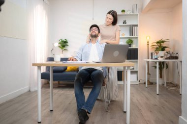 Evde kız arkadaşıyla bilgisayarla çalışırken gülümseyen genç bir serbest çalışanın portresi.