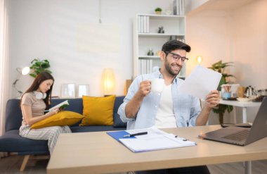 Evde kız arkadaşıyla bilgisayarla çalışırken gülümseyen genç bir serbest çalışanın portresi.