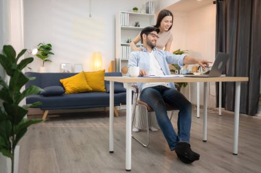 Evde kız arkadaşıyla bilgisayarla çalışırken gülümseyen genç bir serbest çalışanın portresi.